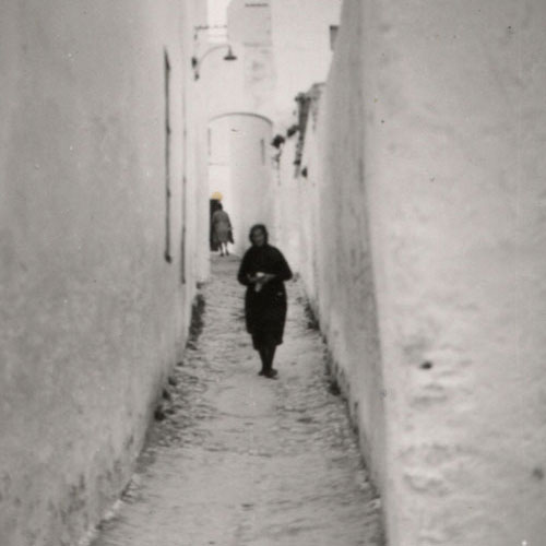 Descripción: Una mujer vestida de negro camina por una calle estrecha encalada en Conil de la Frontera (Cádiz).