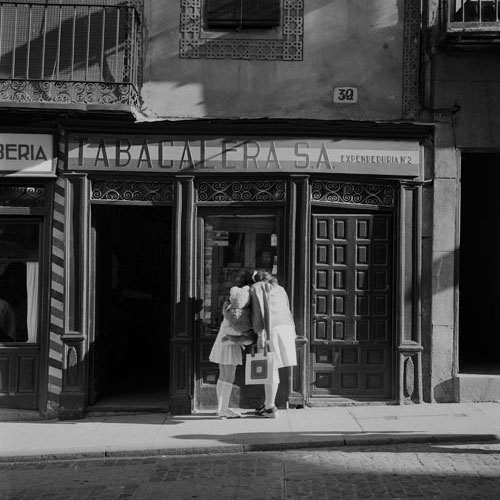 Descripción: Madre e hija, con un peluche, miran el escaparate de una tienda de tabacos en Segovia.
